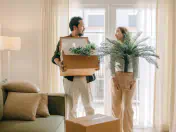 Two people hold houseplants in an apartment